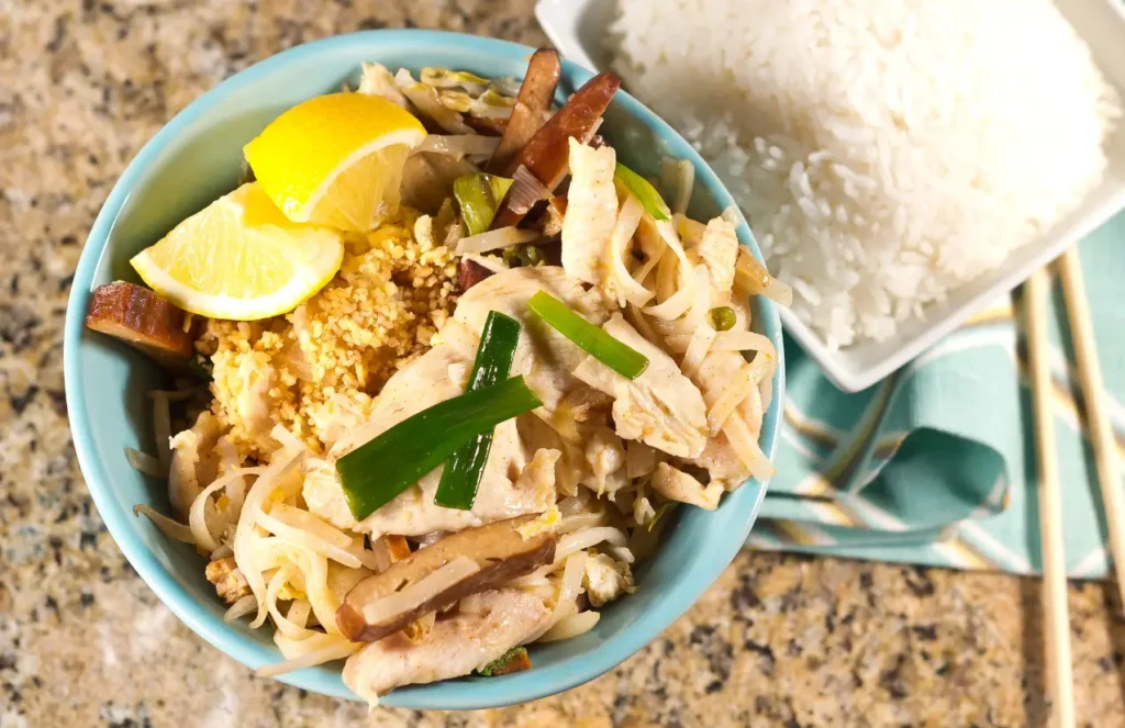 Pad Thaï thaïlandais maison servi dans un bol avec citron vert, cacahuètes et germes de soja