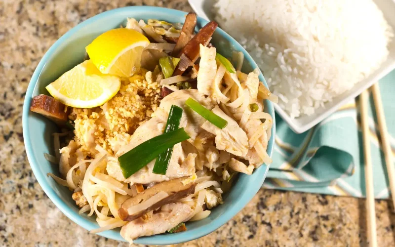 Pad Thaï thaïlandais maison servi dans un bol avec citron vert, cacahuètes et germes de soja